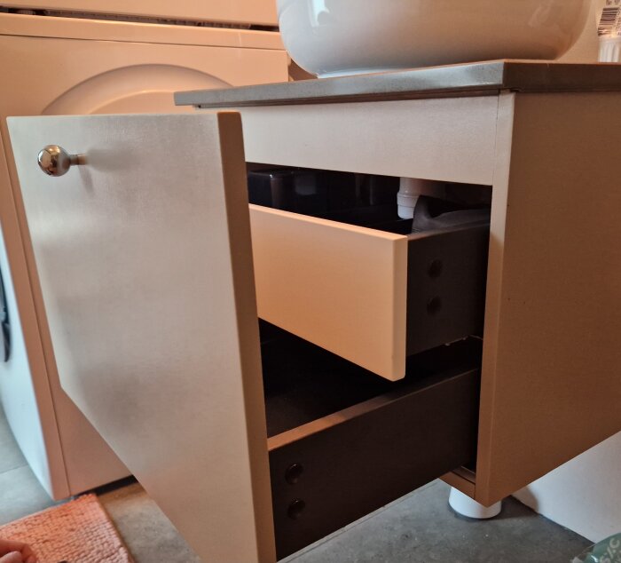 Öppen vägghängd kommod i badrum med synlig låda som behöver lossas. Ingen synlig mekanism för att ta bort lådan.