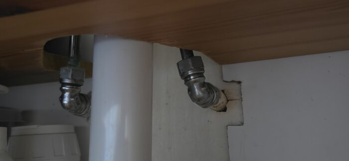 Vattenrör under kommod med metallkoppling, kopplade genom väggen, del av ett hemmafixarprojekt för att byta blandare själv.