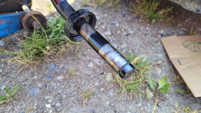 Närbild av en bilaxel utan hjul, synlig dammig mark och lite gräs i bakgrunden. Axelns lager är delvis synliga.