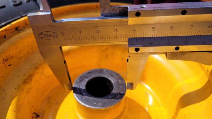 Gult hjul med avlägsnat lager, uppmätt med ett skjutmått som visar cirka 8 cm, sökande efter råd om att byta lager själv.