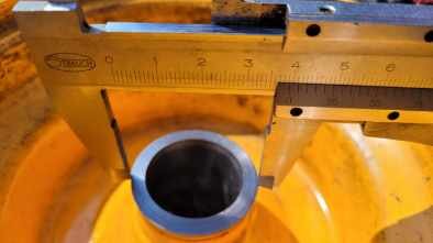 Mätverktyg mäter innerdiametern på ett hjullager. Hjulet ligger i bakgrunden, målade ytor i gult.