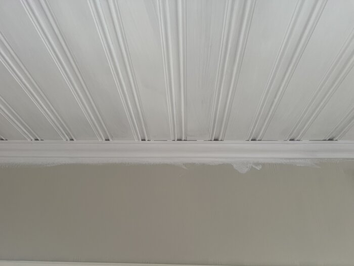 Vitt målat paneltak där det möter en list, med synliga skarvar som kan behöva fogas igen för ett jämnt utseende.