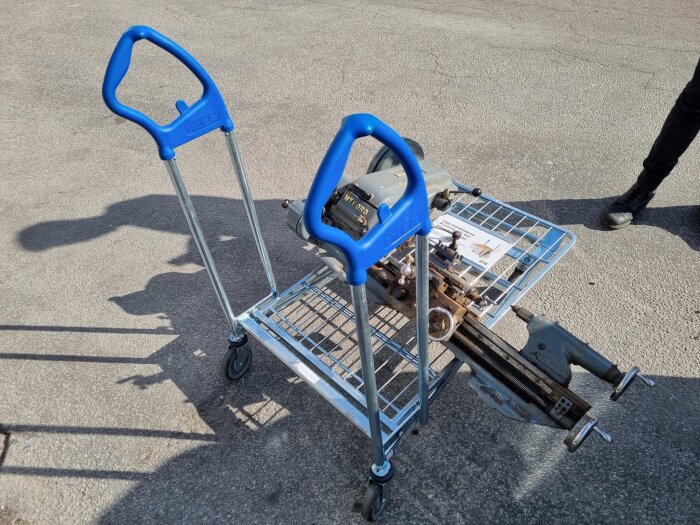 Svarv placerad på en transportvagn utomhus, vagn med blå handtag. En del av svarv och en skugga syns på asfalten.