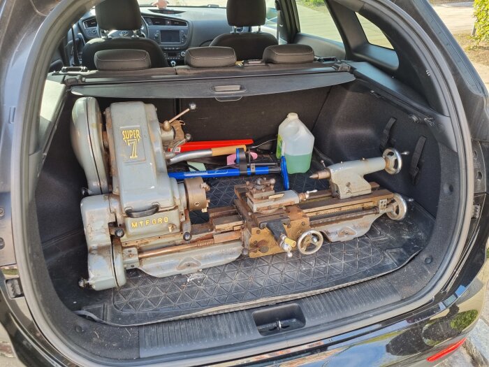 Svarv av märket Myford Super 7 placerad i bagageutrymmet på en bil, omgiven av verktyg och en dunk med vätska.