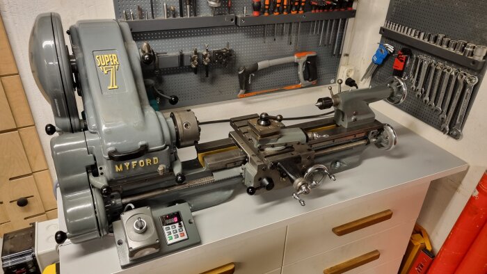 Grå Myford Super 7 svarv på arbetsbänk i en verkstad med verktygshållare och kontrollpanel i förgrunden.