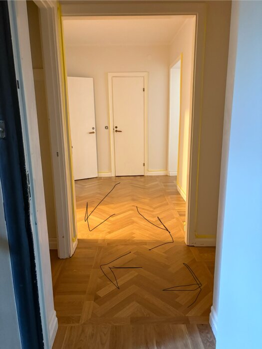 Hall med ny fiskbensparkett som visar asymmetrisk placering av fris vid dörrkarmar, vilket ifrågasätts ur ett estetiskt perspektiv.