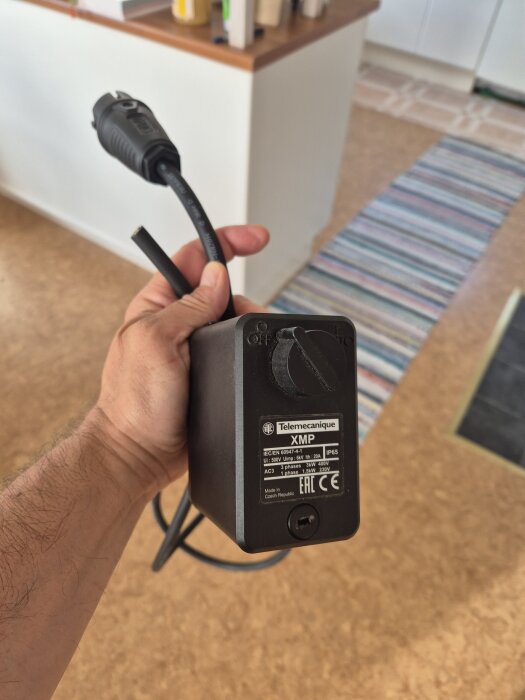 Hand som håller en svart tryckventil från Telemecanique med en stickpropp.