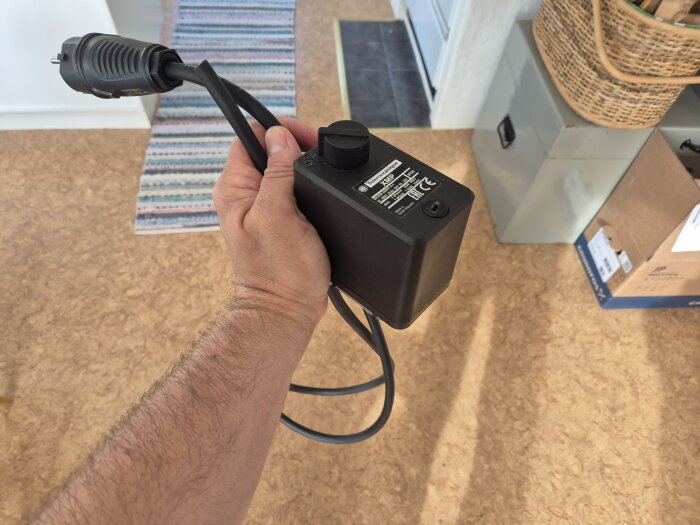 Hand som håller en svart tryckventil med sladd och stickpropp.