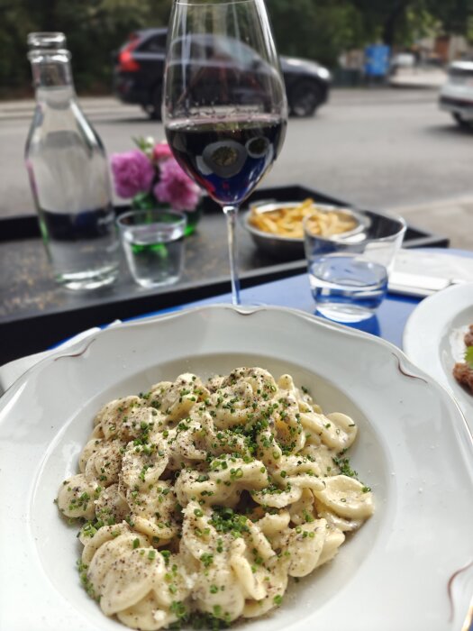 Krämig tryffelpasta toppad med gräslök på en vit tallrik, bredvid ett glas rött vin och en karaff med vatten.