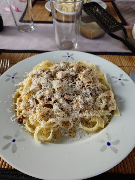 Pasta med kyckling, soltorkade tomater och basilika, toppad med riven ost och svartpeppar, serverad på en vit tallrik.