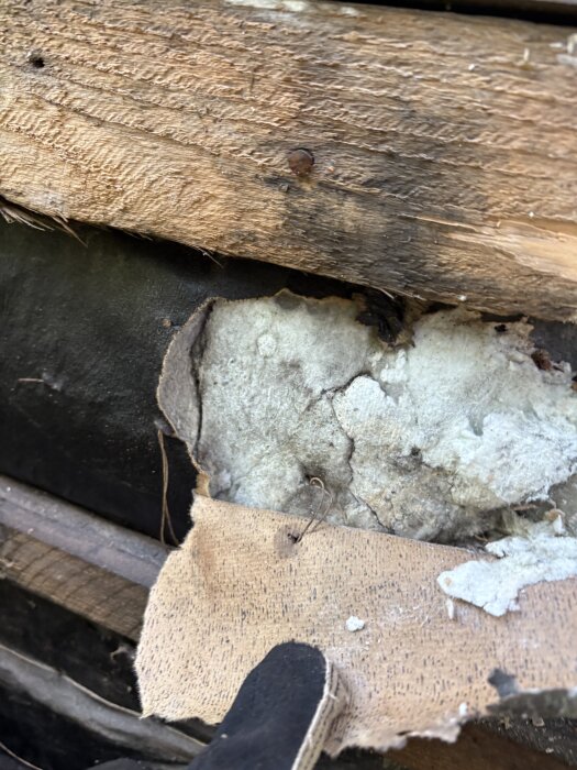 Isolering under ytterpanel på husvägg med synlig träram och skadad yta, misstänkt innehåll som kan innehålla asbest.