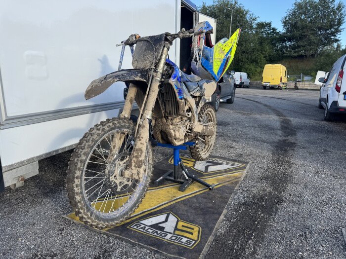 Blöt och lerig motocrossmotorcykel står på ett ställ utomhus efter två dagars hällregn.