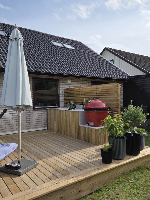 Nybyggd altan med röd grill i hörnan, omgiven av växter i krukor, bredvid ett hus med tegelväggar och fönster.