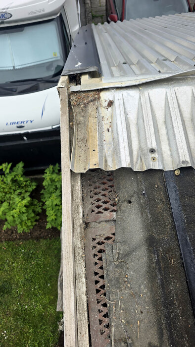 Gammalt trapetstak avlägsnat, visar skadad takpapp och brädor på garage, med ny plåt ovanpå. Slitage och rost syns tydligt på materialet.