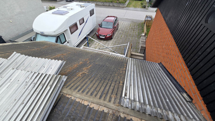 Takfallet med plåtdelar ovanför en källartrappa, en stege vid sidan och en husvagn och bil som står parkerade på uppfarten.