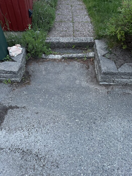 Gångväg med betongtrappsteg och omgivande gräs, en leksaksnalle till vänster på muren.