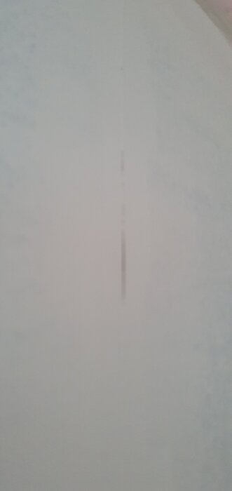 Närbild av en vitmålad vägg med synliga tapetskarvar efter två lager färg.