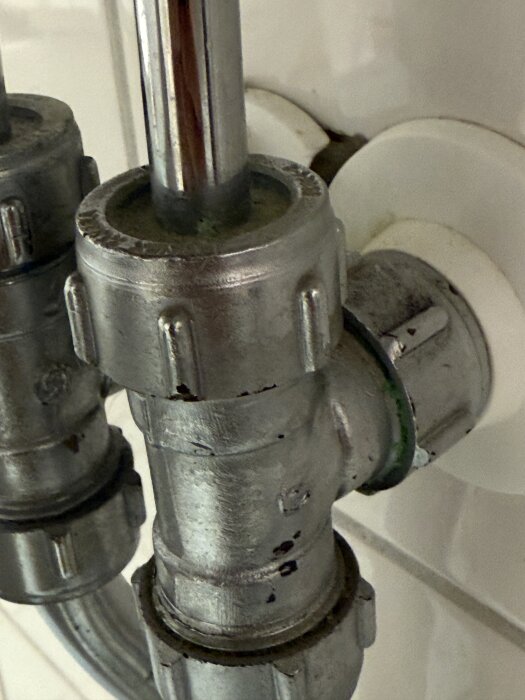 Närbild av en metallisk VVS-koppling under en diskbänk med målade ytor och synliga skruvmönster.