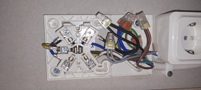 Eluttag med flera kablar anslutna till terminaler. Flera ledningar i olika färger, inklusive brun, blå och grön/gul. Perilex-koppling synlig.