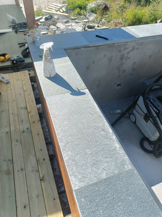 Bild på ett pooldäck under konstruktion med verktyg och material runtomkring samt en stödmur med cortenplåt.