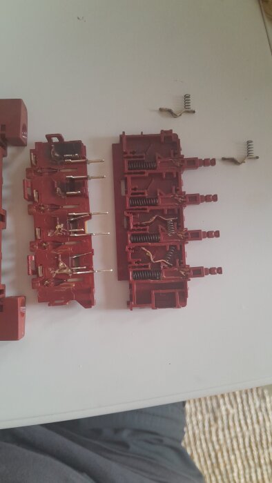 Röd knappsats med metallkontakter och fjädrar, delvis isärplockad och placerad på ett bord.