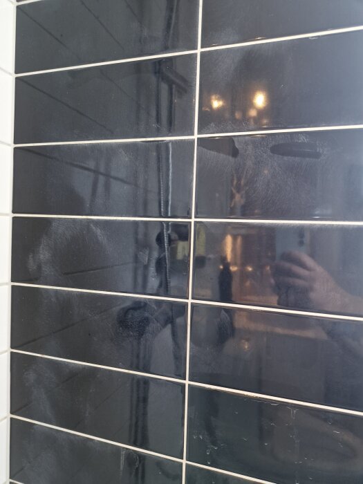 Svart kakelvägg i badrum med synliga dammfläckar och ljusare fogar efter rengöring med mögelborttagningsmedel och citronsyra.