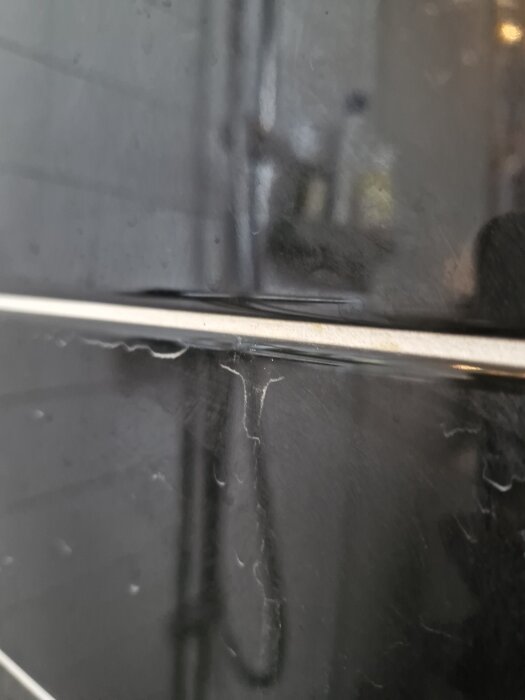 Närbild av kakelplattor i ett badrum där fogarna har börjat lossna och lämnat vita dammfläckar på den svarta kakelytan.