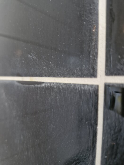 Närbild av svarta kakelplattor med ljusa fogar som lossnar och efterlämnar vita dammfläckar.