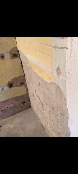 Källarvägg med synlig puts och hålsten, delvis borttagen puts och gulmålad yta, visar renoveringsarbete i tvättstuga.