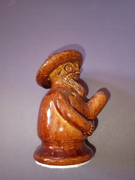 En brun lergök med originell och ekivok form, föreställande en figur med hatt och skägg, visas i profil.