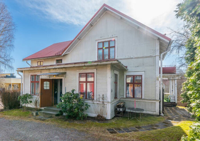 Vit gammal villa med rött tak och trädgård. Huset har stora fönster, en öppen dörr och står på en stengrund.
