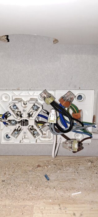 Elcentral med flera kablar och kopplingar, en vit avklippt sladd syns tydligt och dammigt golv. Lös koppling till perilex och ugnsuttag.
