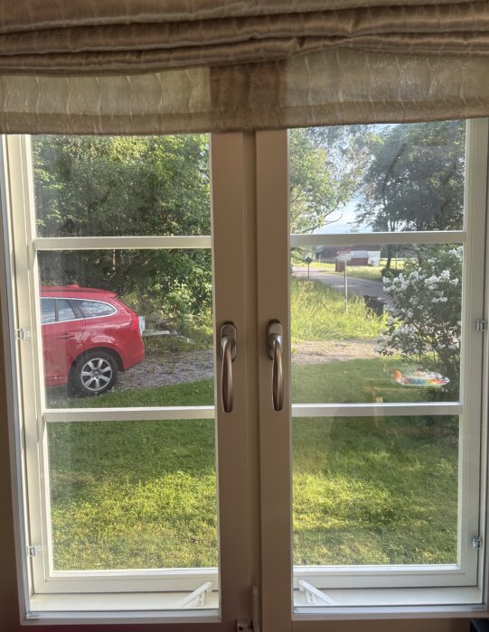 Nya fönster med moderna handtag och utsikt mot en grönskande trädgård, där ägaren överväger att byta till tidsenliga spanjoletter.