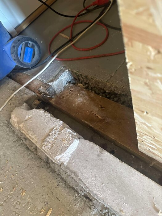 Betonggolv med träplanka och anslutande kablar, förberett för flytspackling och dörrkarm.
