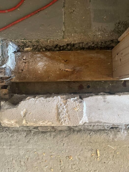 Betonggolv med träbjälkar och röda kablar syns på en byggarbetsplats där flytspackling förbereds inför montering av dörrkarm.