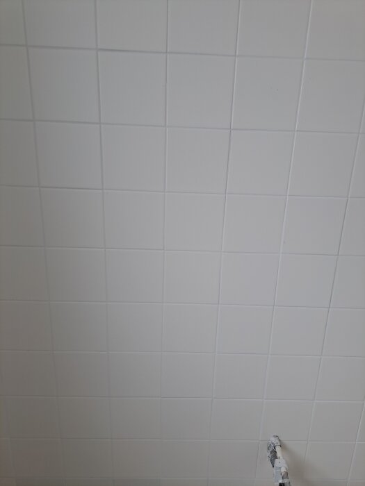 Vitt kakel på en vägg, med jämn yta för vattenpass, syns tillsammans med en del av ett rör i nedre delen av bilden.