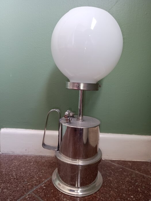 Karbidlampa med vit glaskupa och metallbas, användes som alternativ till fotogenlampor. Ventilen på sidan reglerar vattenflödet för gasproduktion.