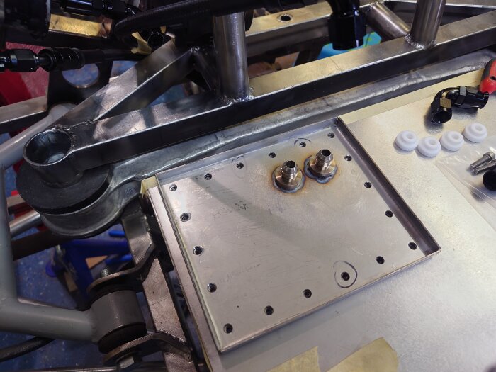 Montering av metalldelar med donkopplingar och skruvar, omgiven av verktyg och vita plastbrickor.