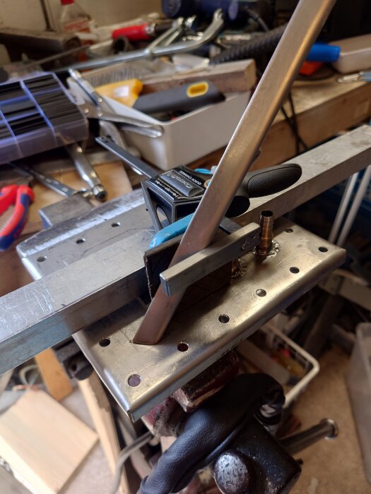 En arbetsbänk med verktyg, metallbitar och en tving. Verkstadsprojekt pågår.