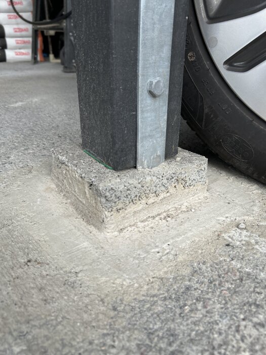 Plint i carport med metallstolpe och närliggande bildäck, visar kvaliteten på betongarbetet.