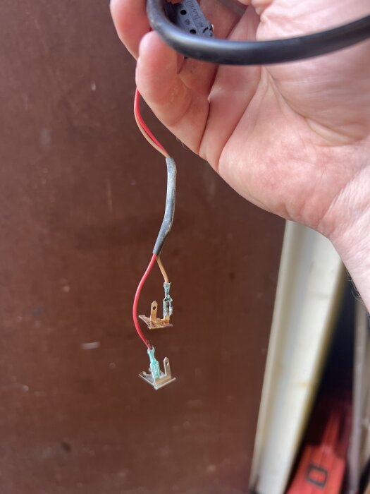 Hand håller nya metallkontakter med röda och bruna kablar för glödlampa till nummerskyltsbelysning. Används för att ersätta gamla kontakter.