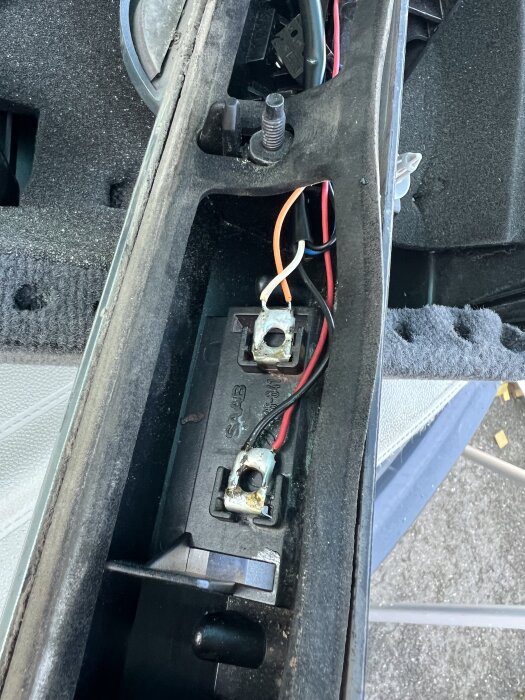 Kontakter för nummerskyltsbelysning med metallband och kablar inuti ett fordon under reparation av glödlampa.
