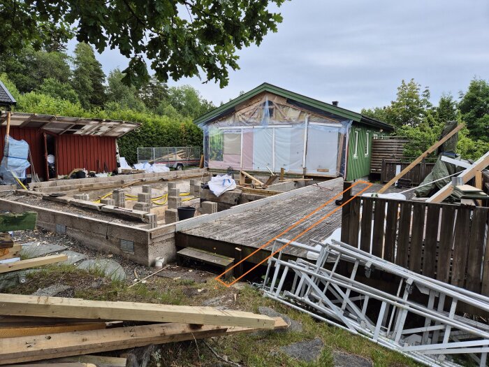 Riven husgrund under ombyggnad, med befintlig krypgrund synlig och markerad med orange linjer där ny breddning planeras med plintar eller mur.