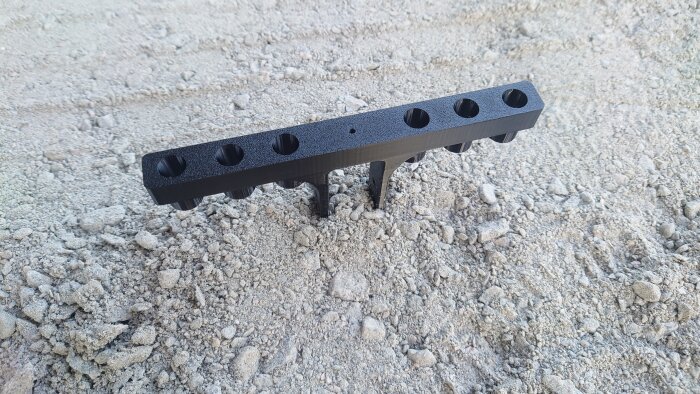 Svart plastmonteringshållare för högtryckstvättsmunstycken med flera hål, placerad på grus.