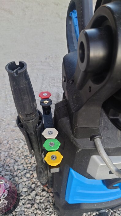 Högtryckstvätt med munstyckshållare med fyra färgglada munstycken fastsatta, monterad på grusunderlag.