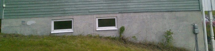 Bild av en suterränghusvägg med små växter nära fönster, några ventilationsöppningar, och gräsmatta täckt område.