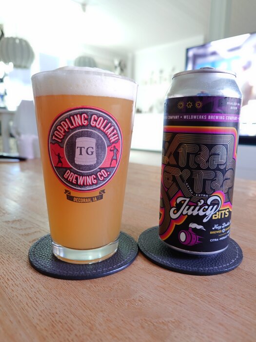 Ett glas med öl från Toppling Goliath Brewing Co. och en burk Juicy Bits från Weldwerks Brewing Company på ett bord i ett hem.