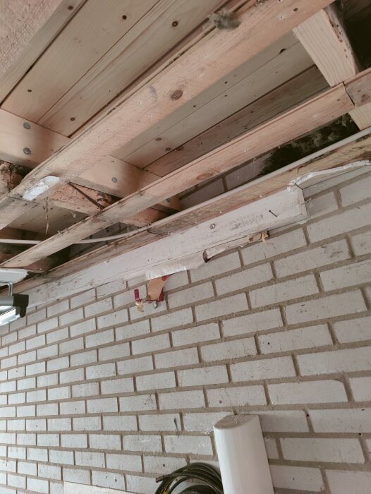 Träbjälklag och tegelvägg under byggnation, fack med ventilationshål planeras för luftspalt mot yttervägg.