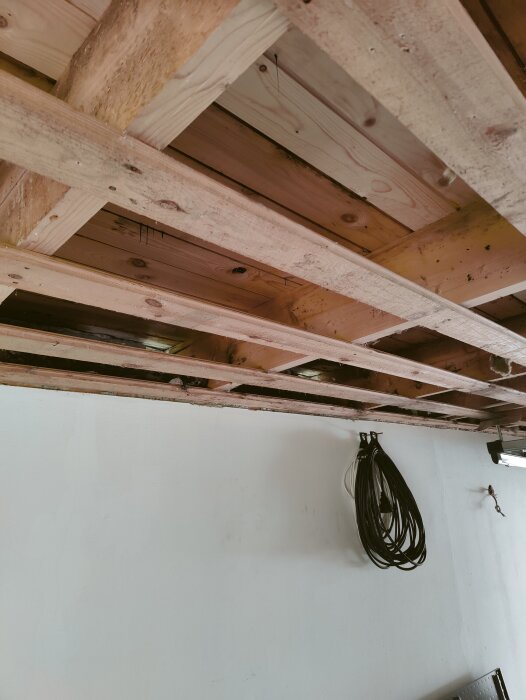 Trätakstolar med synliga balkar i ett byggprojekt, väggen med hoprullad kabel syns också.