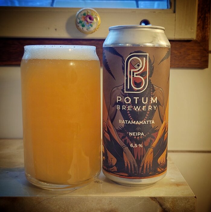 En burk Potum Brewery NEIPA Ratamahatta 6,5% bredvid ett glas med fylligt gul öl, placerad på en marmoryta.